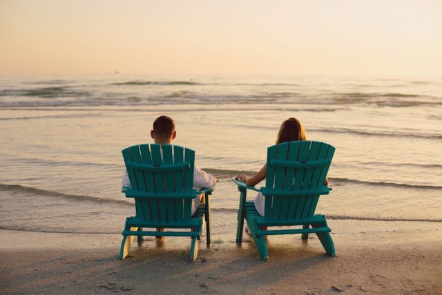 Two people sitting in Wildridge Adirondack chairs on the beach